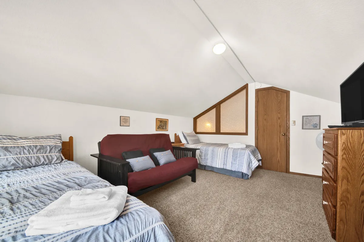 A spacious upstairs room with two beds, a sofa bed, a chest of drawers, and a sloped ceiling – designed as a fun, flexible hangout and sleeping space for kids or teens. The room is both playful and comfortable, offering space for relaxation and bonding.