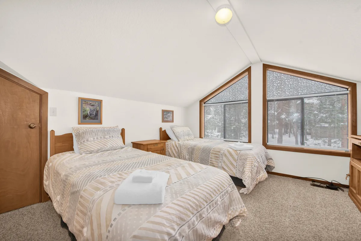 A serene bedroom with twin beds, large windows offering a snowy landscape view, and classic wooden furniture. The setting is peaceful, with space for reading, relaxing, and enjoying the scenery.