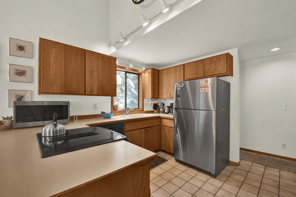 A modern kitchen with a central island, stainless steel appliances, wooden cabinets, and a large window letting in natural light. The open layout invites meal prep, socializing, and easy flow to adjacent living spaces.
