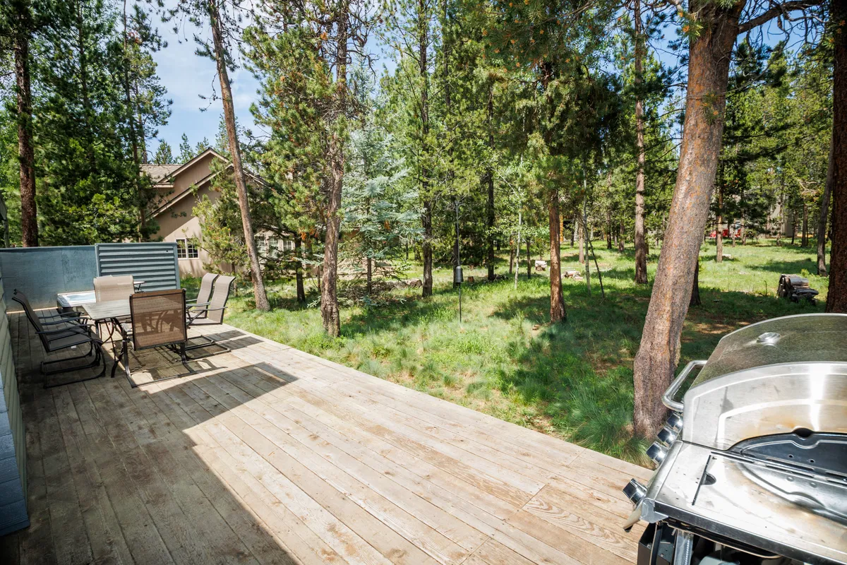 This image focuses on the outdoor dining set and grill located on the deck, with views of the surrounding trees. The setup is ideal for barbecuing, sharing meals outdoors, and soaking in the natural environment, echoing the features highlighted in the section.