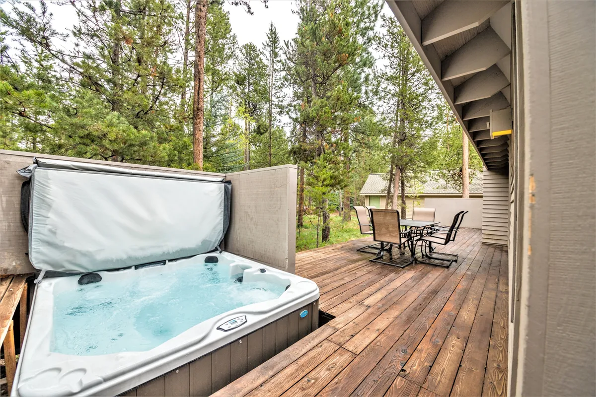 A wooden deck surrounded by trees, featuring a hot tub, outdoor seating, and a dining area. The space seamlessly connects to the home's interior, inviting relaxation and outdoor meals.