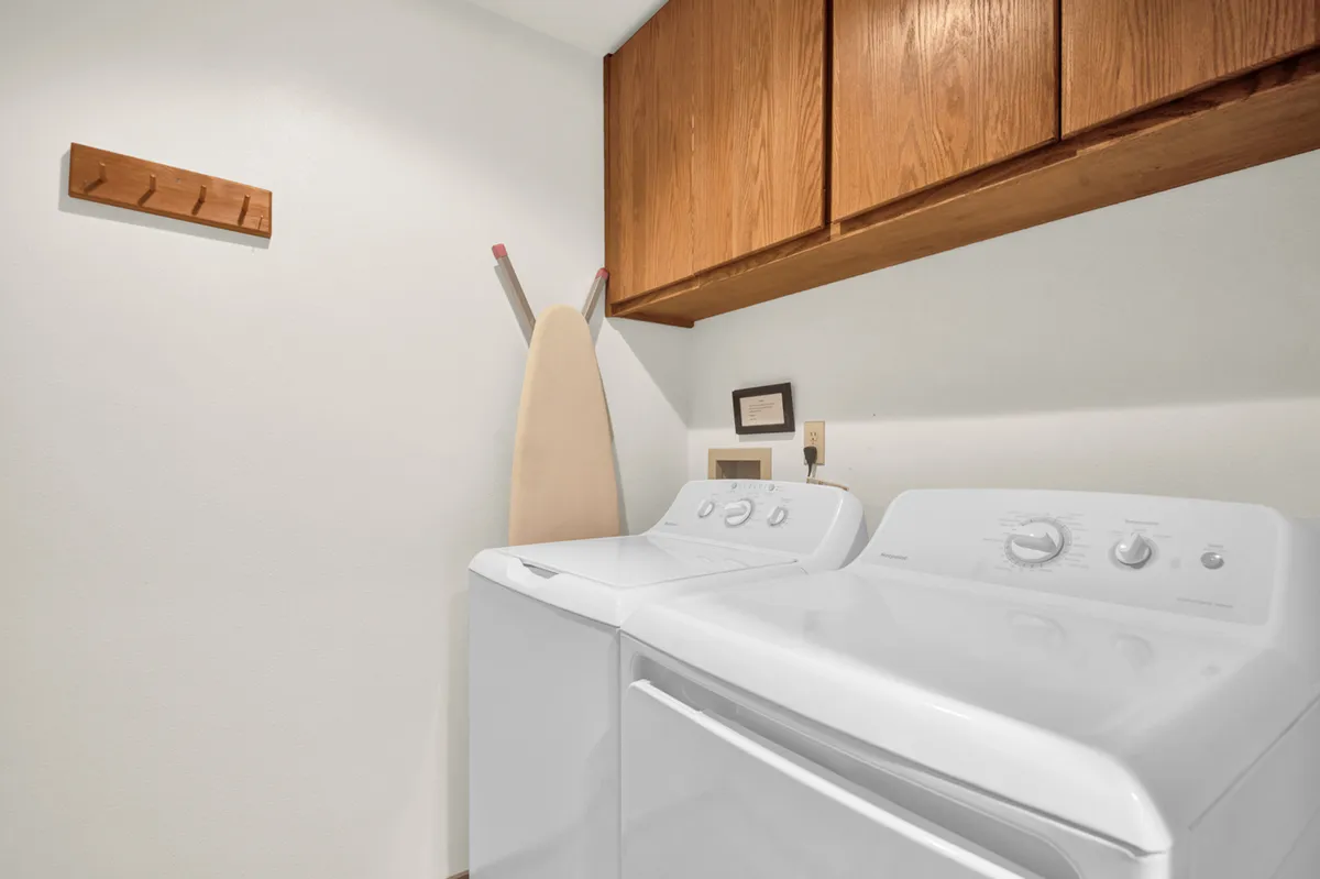 This image features a practical, well-organized laundry room with a washer, dryer, ironing board, and wooden shelving. The space is tidy, functional, and designed for convenience, supporting easy laundry tasks during your stay.