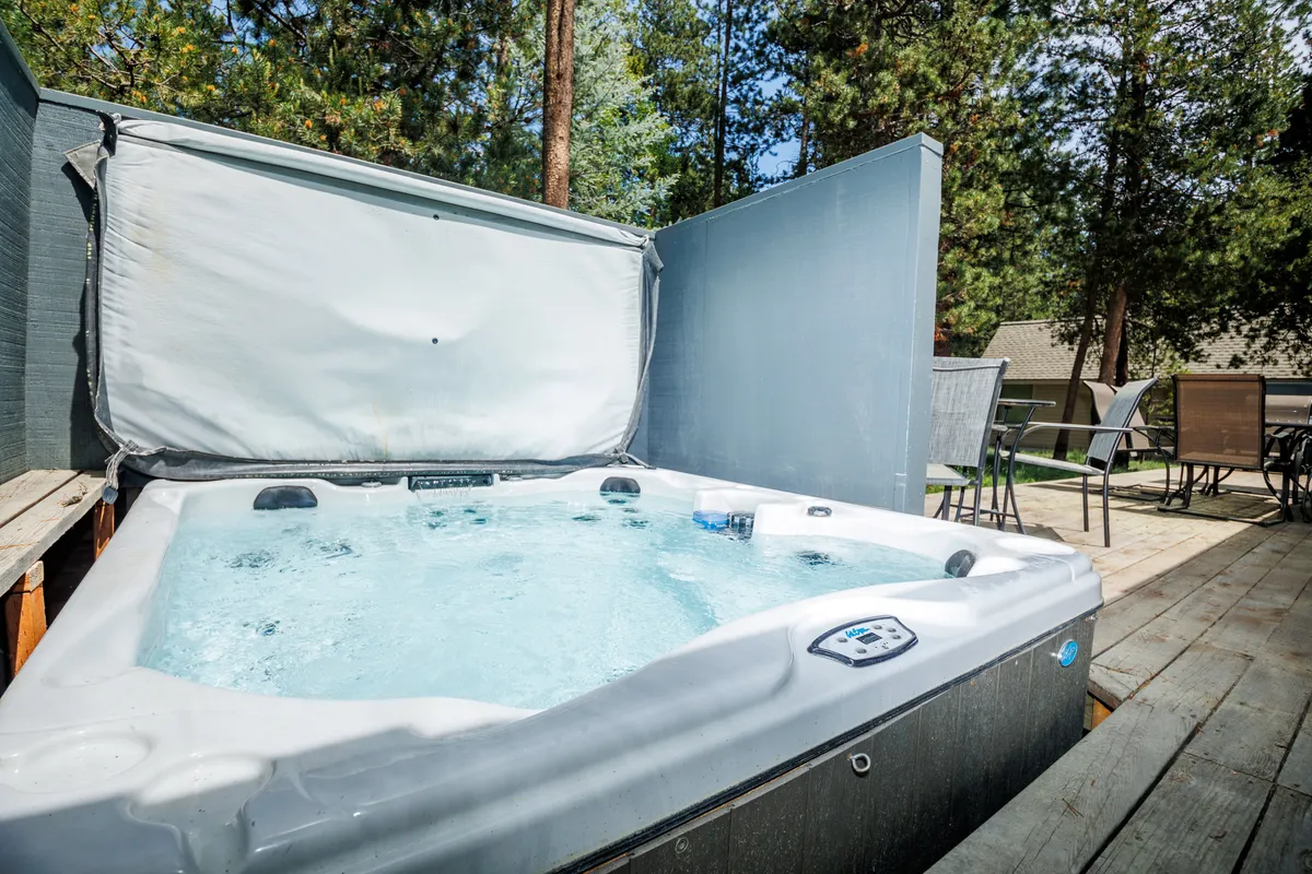 A bubbling hot tub nestled on a private patio, surrounded by pine trees and comfortable patio furniture. The serene backyard atmosphere invites relaxation and stargazing after a full day of activities.