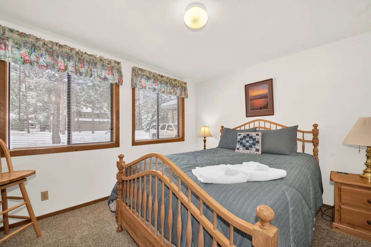 An inviting bedroom with a neatly made bed, large windows revealing a snowy view, a nightstand with a lamp, and a cozy atmosphere perfect for relaxation and reading.