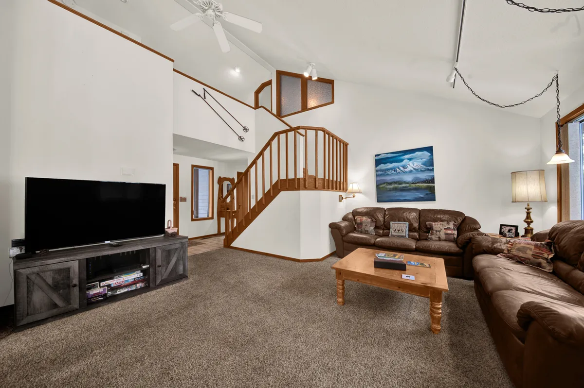 The image showcases a warm and inviting living room with plush sofas arranged around a sleek coffee table, a staircase leading to the upper level, a large television, and tasteful artwork adorning the walls. The space is designed for relaxation and gathering, with soft lighting and an open, airy feel that encourages both cozy movie nights and festive family celebrations.