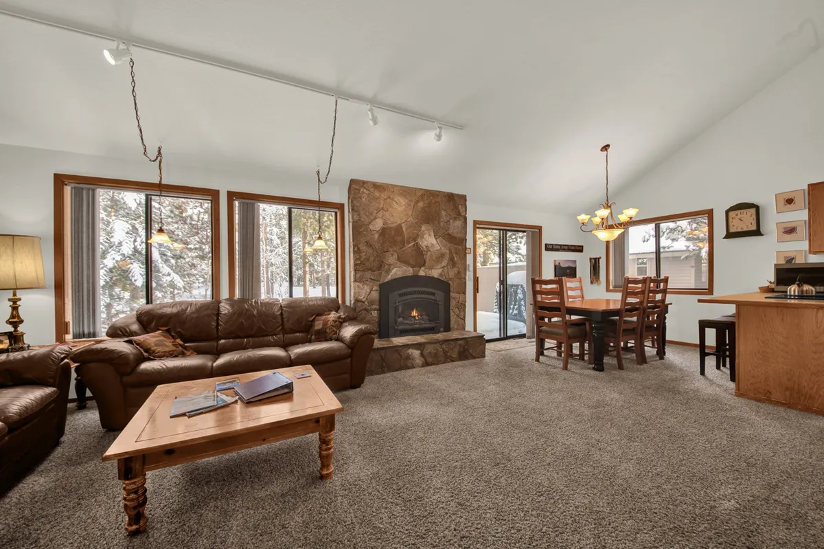 A warmly lit living room anchored by a cozy fireplace, a comfortable sofa, and a spacious dining table nearby. The open-concept layout showcases both the living and dining spaces, with ample room for families to relax or gather for meals.