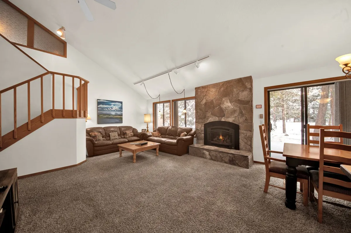 A warm, inviting living area featuring a cozy fireplace, comfortable sofa, a spacious dining table, and a staircase leading to the upper level. The space is designed to encourage gatherings for family game nights, relaxing evenings by the fire, or shared meals in a homey setting.