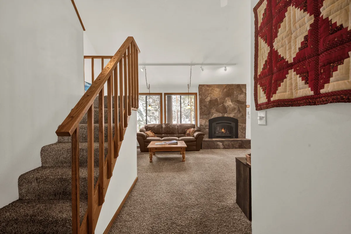 A cozy sitting area is highlighted, showing a staircase, a plush sofa, a glowing fireplace, and a quilted wall hanging. The space invites relaxation, reading, and quiet moments after a day of adventure, with a balance of homey comfort and style.