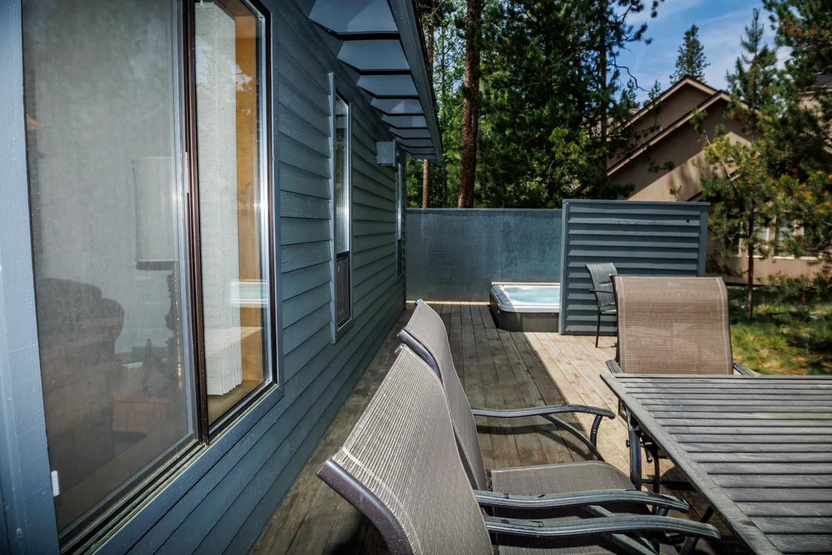 This image features a spacious outdoor seating area on the back deck, complete with a dining table and a private hot tub nestled nearby. Surrounded by trees, the deck offers views of the natural landscape and plenty of privacy, capturing the tranquil outdoor ambiance described in the section.